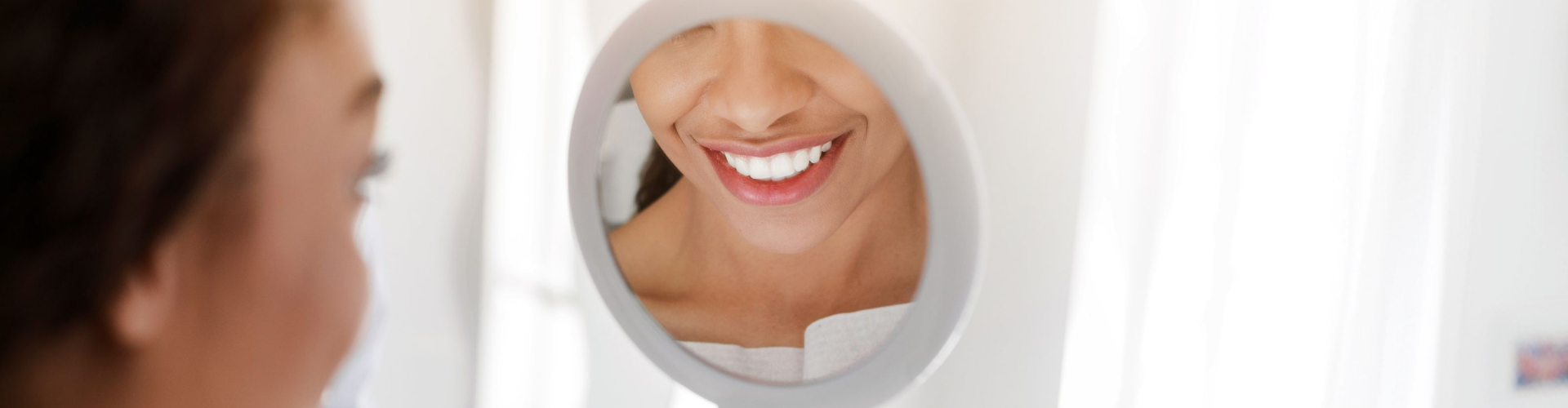 Smiling dental patient admiring her bright, healthy smile in a mirror after cosmetic dental treatment.